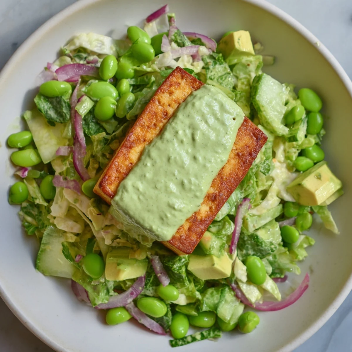 The fresh Green Goddess Salad showcases vibrant green herbs, edamame, and sugar snap peas tossed in a creamy dressing.