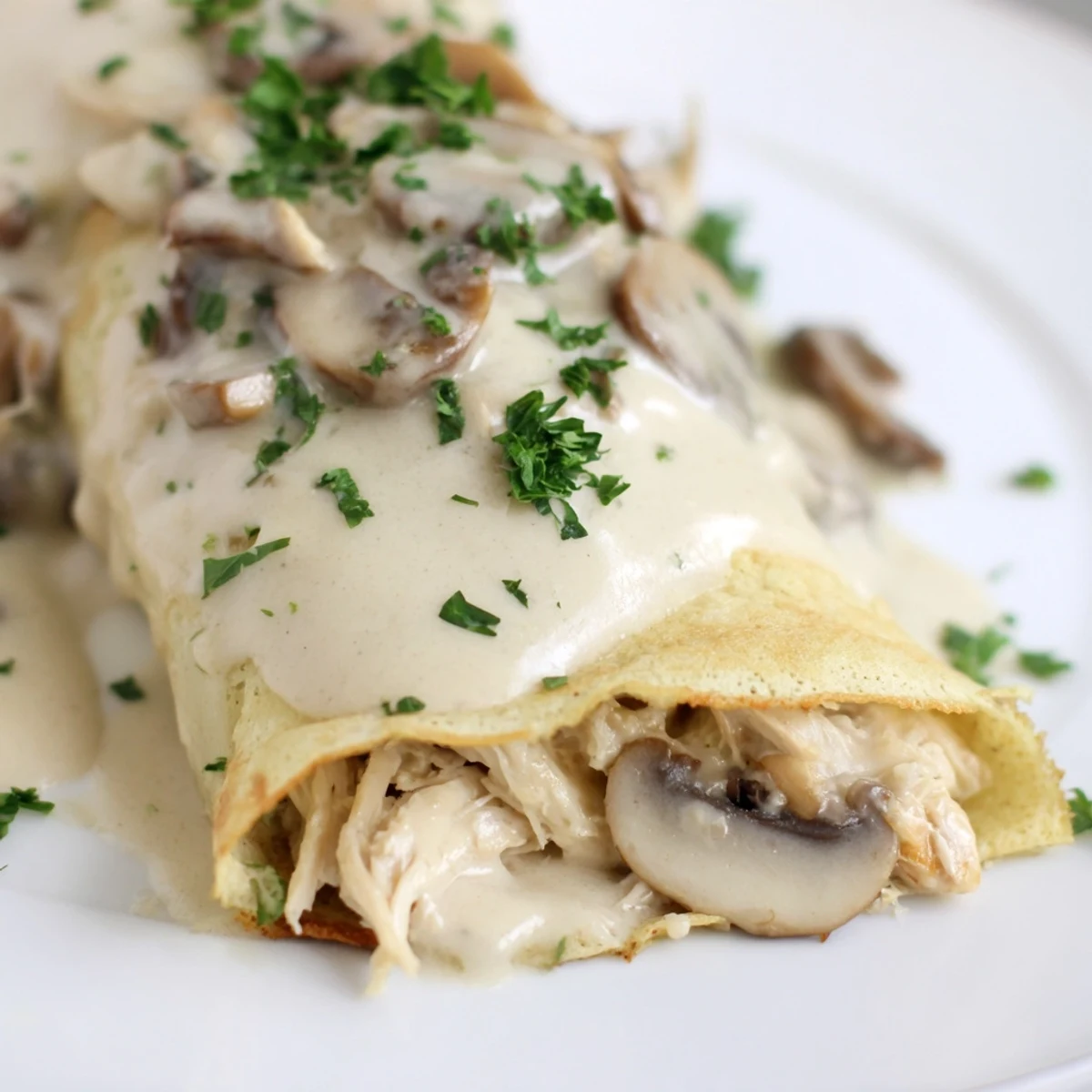 Savory crêpes with tender chicken and rich mushroom sauce on a white plate.