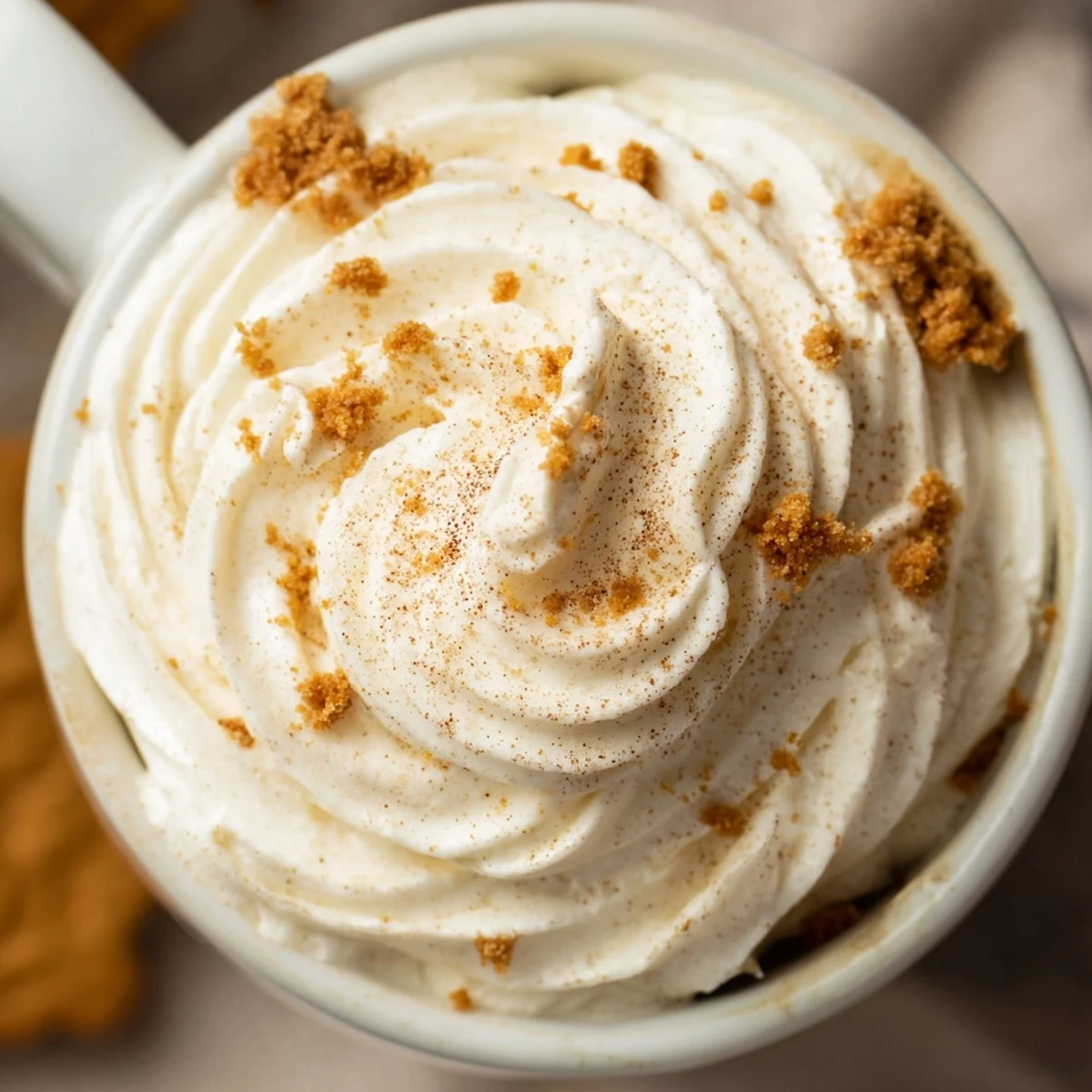 Two warm gingerbread lattes topped with whipped cream, served with gingerbread cookie crumbs.