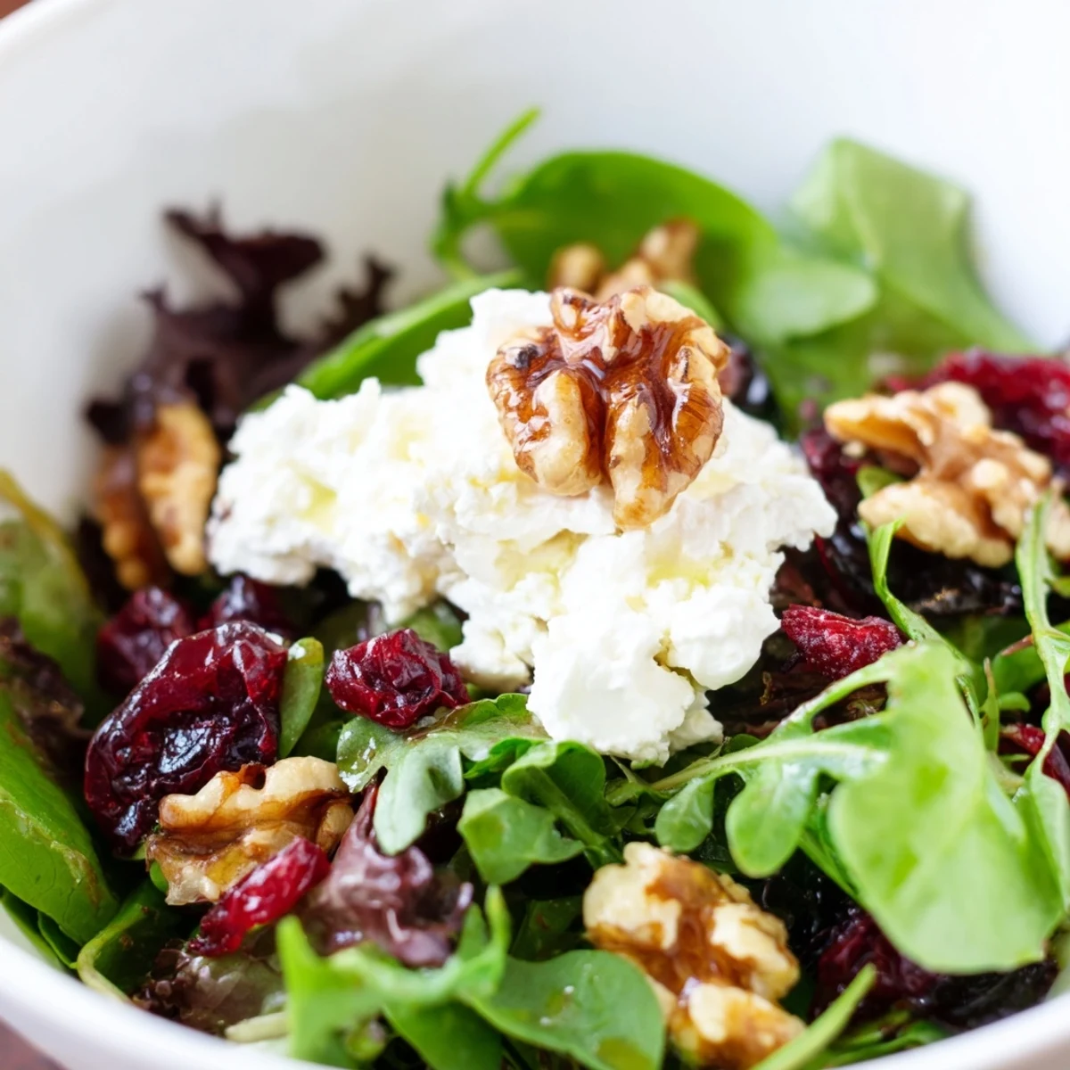 In a rustic ceramic bowl, this easy Cranberry Walnut Salad combines mixed greens, tangy goat cheese crumbles, and sweet cranberries, ready to be tossed with a honey-Dijon vinaigrette.