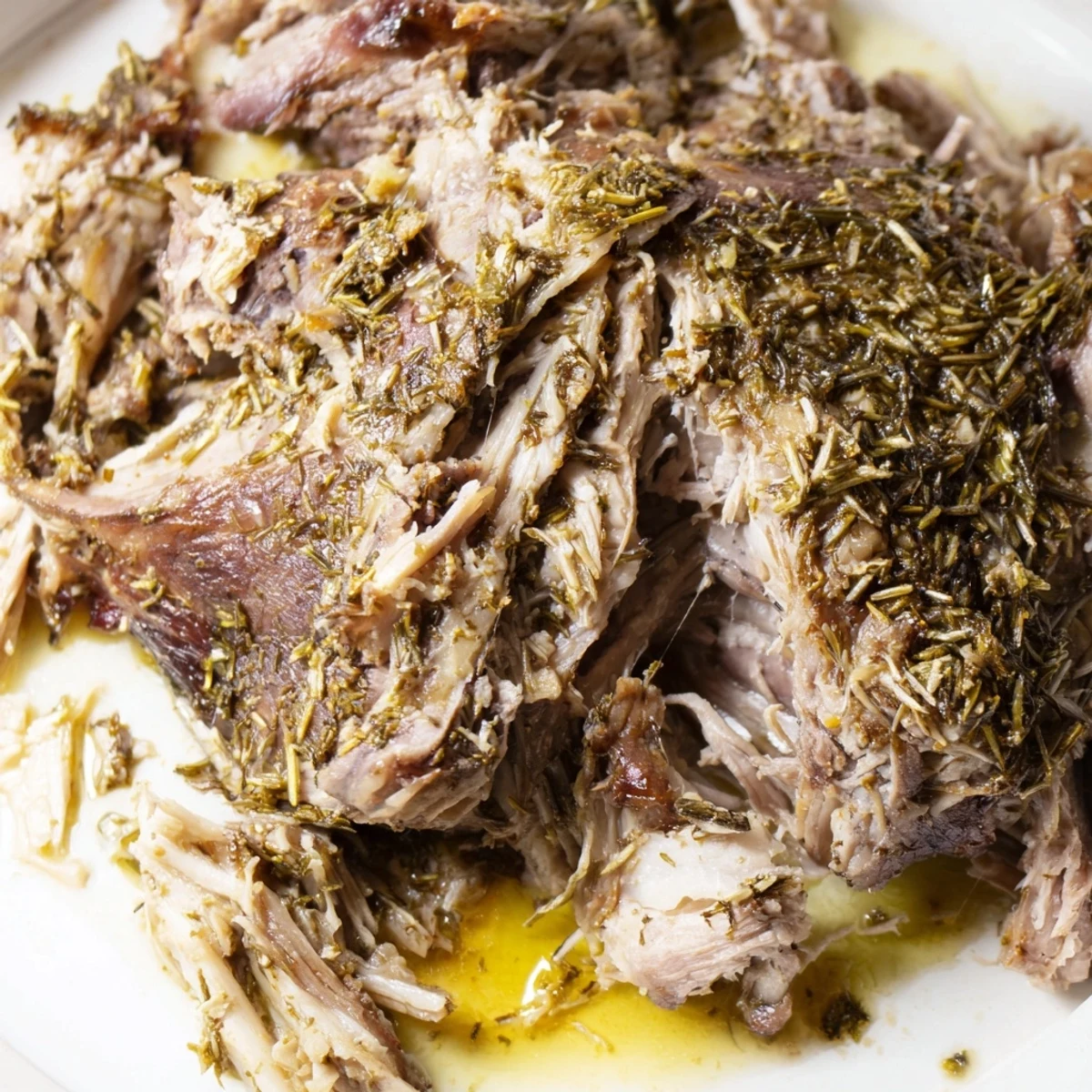 Family-style platter of slow roasted lamb shoulder with herbs, glistening with savory drippings and paired with crusty bread.