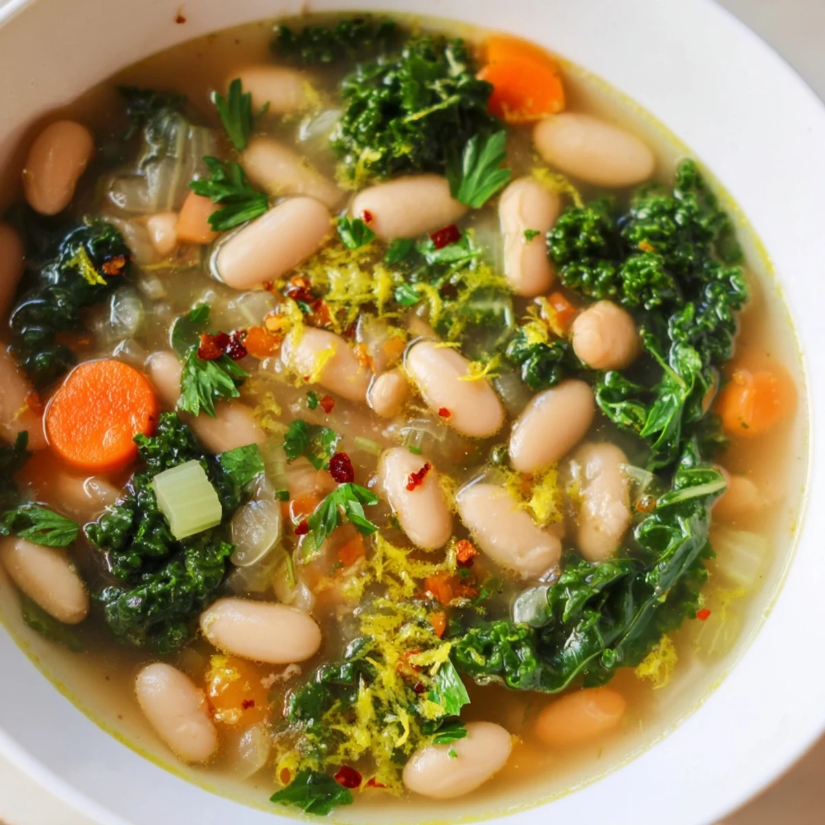 Tender white beans and chopped kale simmer in a savory broth with bright lemon zest, ready to be ladled into rustic bowls.