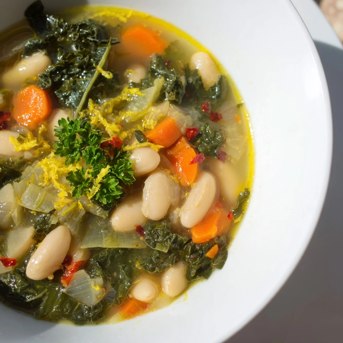 A steaming bowl of White Bean and Kale Soup with Lemon Zest sits beside a slice of crusty bread, perfect for a cozy lunch.
