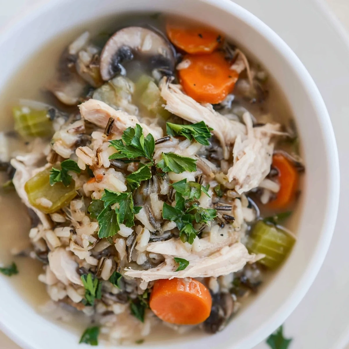 A ladle of hearty Instant Pot Chicken and Wild Rice Soup over fresh spinach, served with a slice of crusty bread.