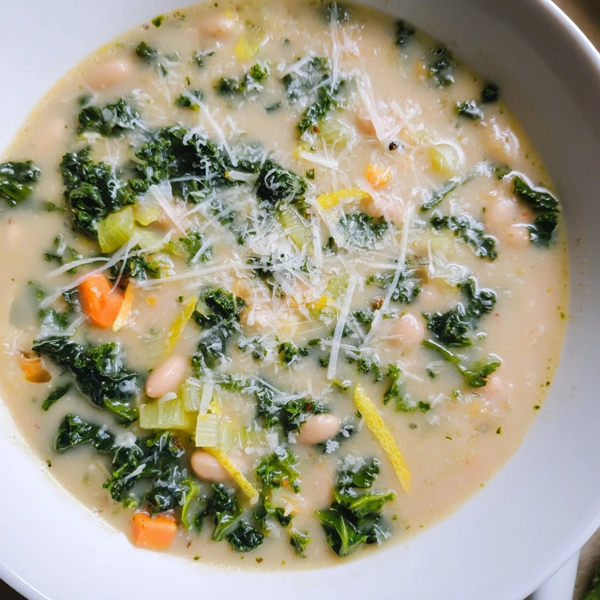 Hearty White Bean and Kale Soup with Lemon Zest and Parmesan garnished with parsley and extra cheese, served with crusty bread.