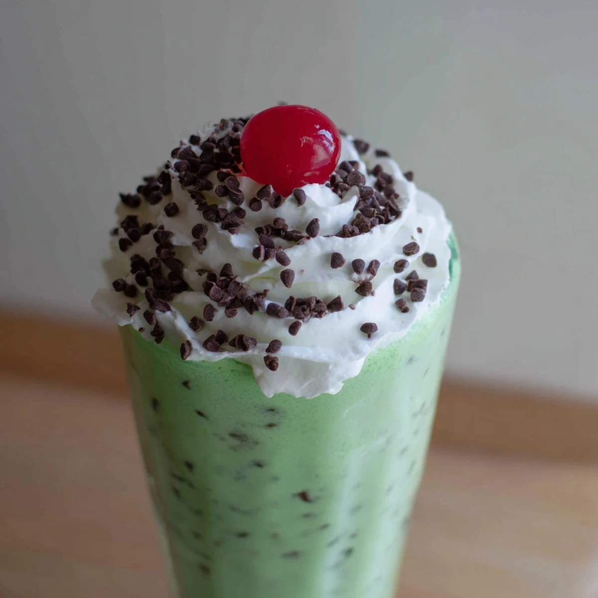 Cold, refreshing Shamrock Mint Chocolate Chip Milkshake poured into a tall glass, with minty aroma and chocolate chips.