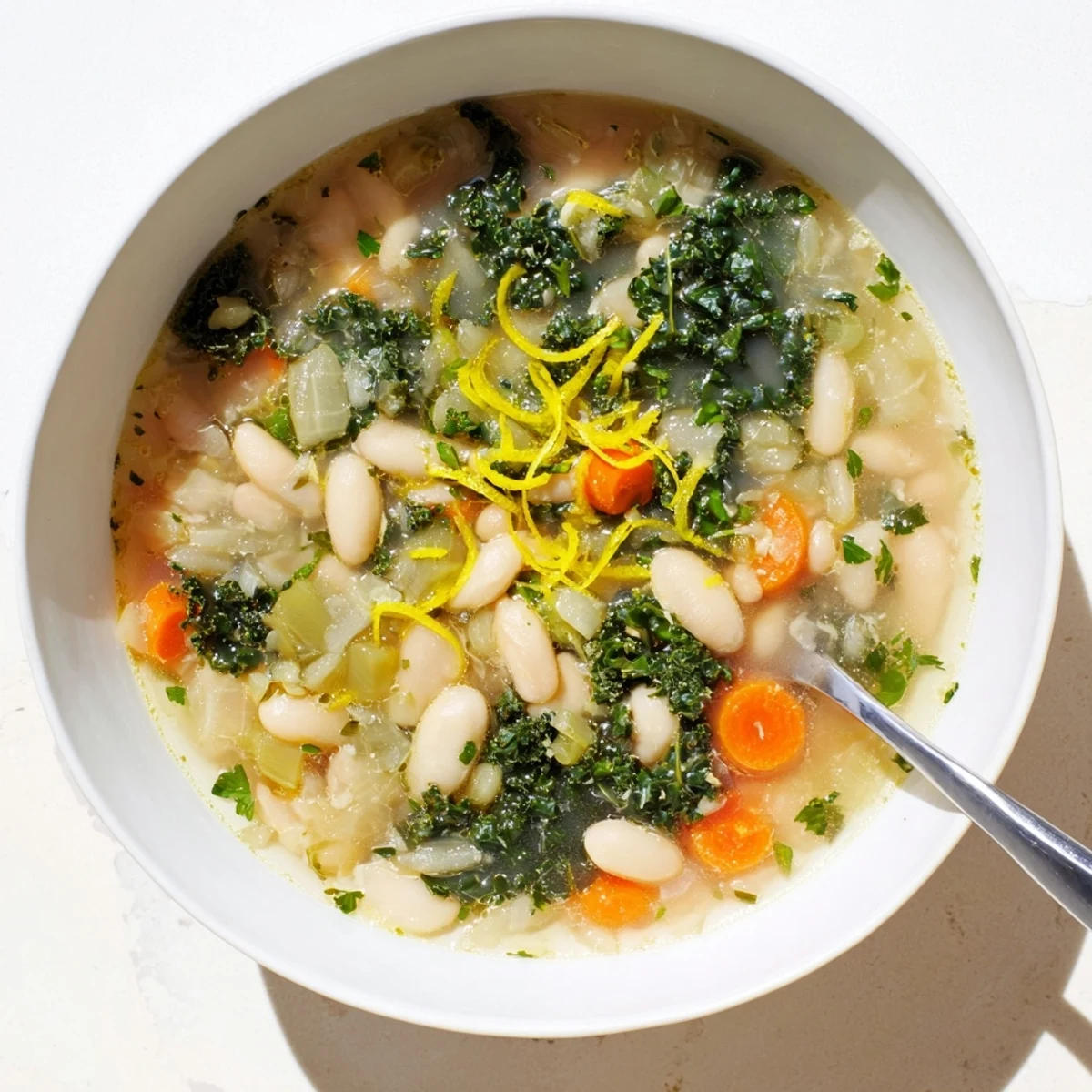 Hearty White Bean and Kale Soup with Lemon Zest steaming in a rustic bowl, topped with fresh parsley and grated Parmesan.