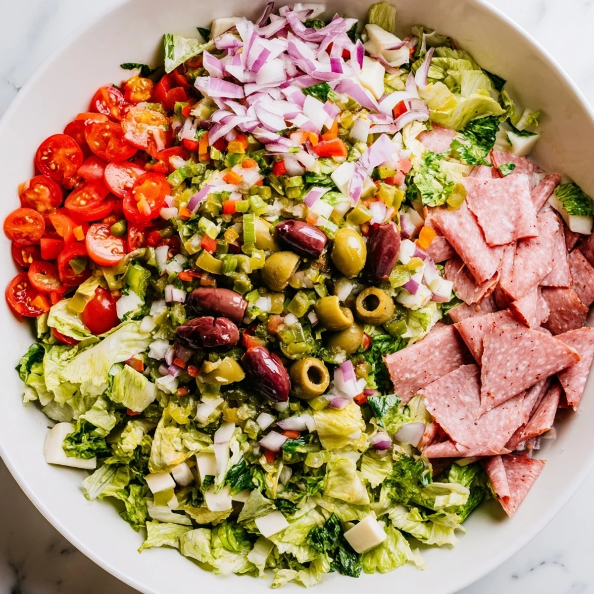 Crisp romaine and iceberg lettuce tossed with vibrant cherry tomatoes, red onion, and a bold New Orleans Muffuletta Salad featuring olives, salami, and provolone.
