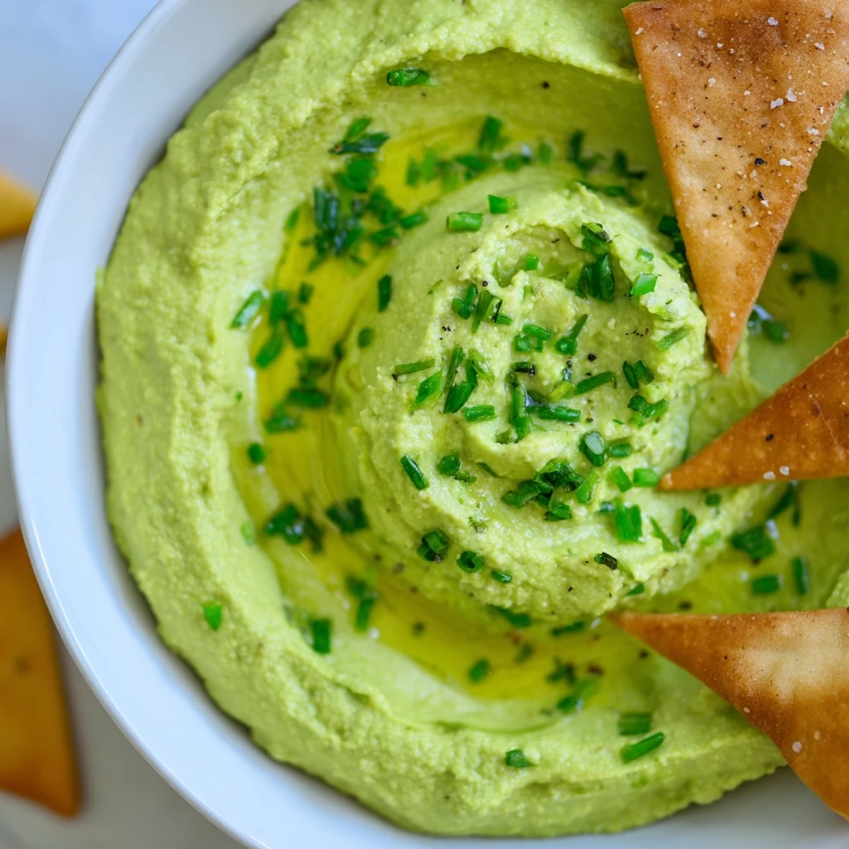 Vibrant Green Avocado Hummus served with crispy, golden-baked whole wheat pita chips for dipping, perfect for a party appetizer.