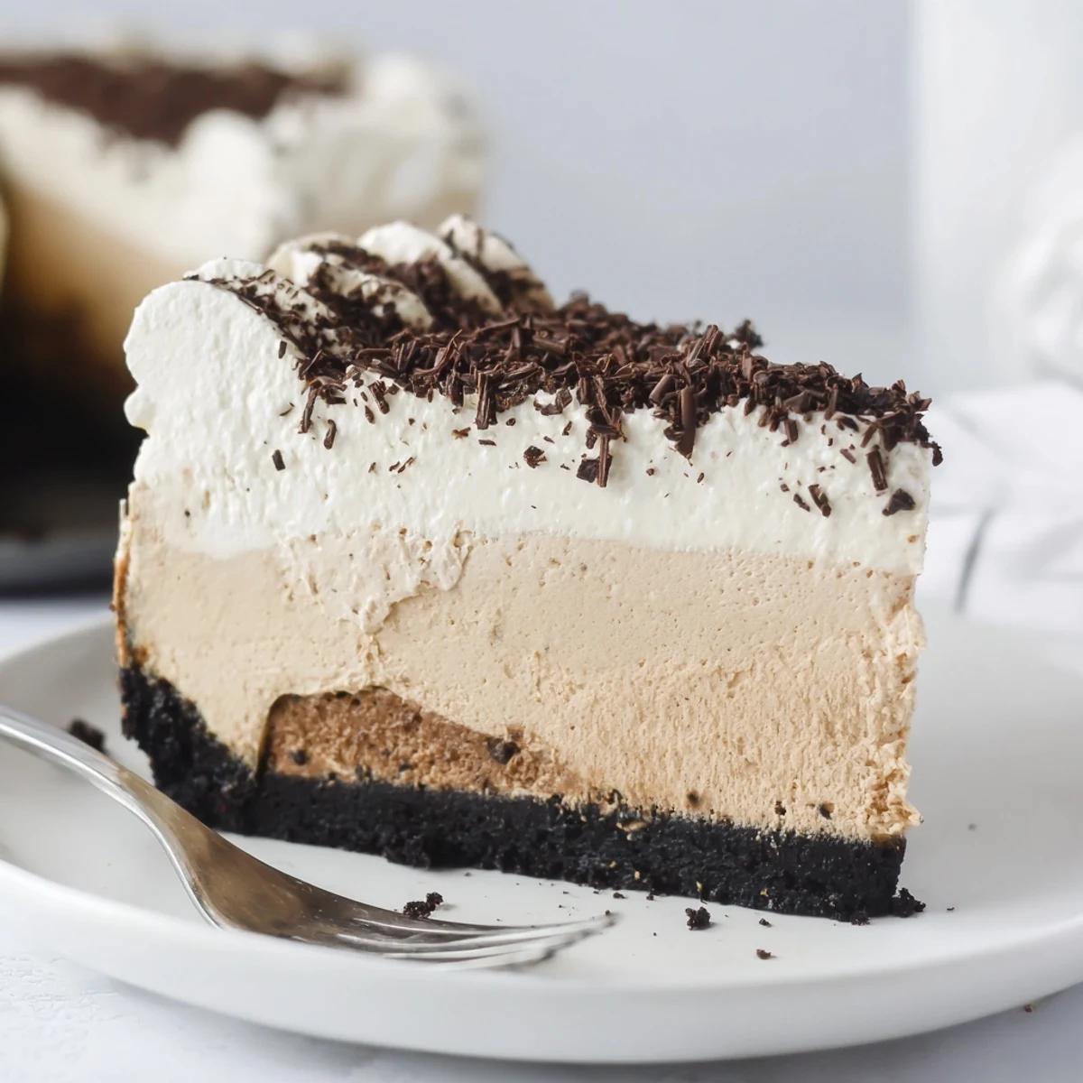 A rich slice of Irish Cream Cheesecake on a white plate, topped with fluffy whipped cream and dark chocolate shavings for an indulgent, festive dessert.
