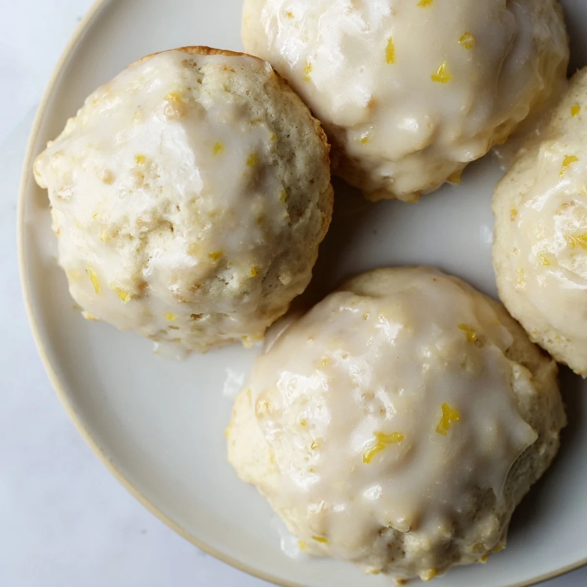 Freshly baked Lemon Ricotta Cookies with a shiny lemon glaze, arranged on a cooling rack over a marble countertop.