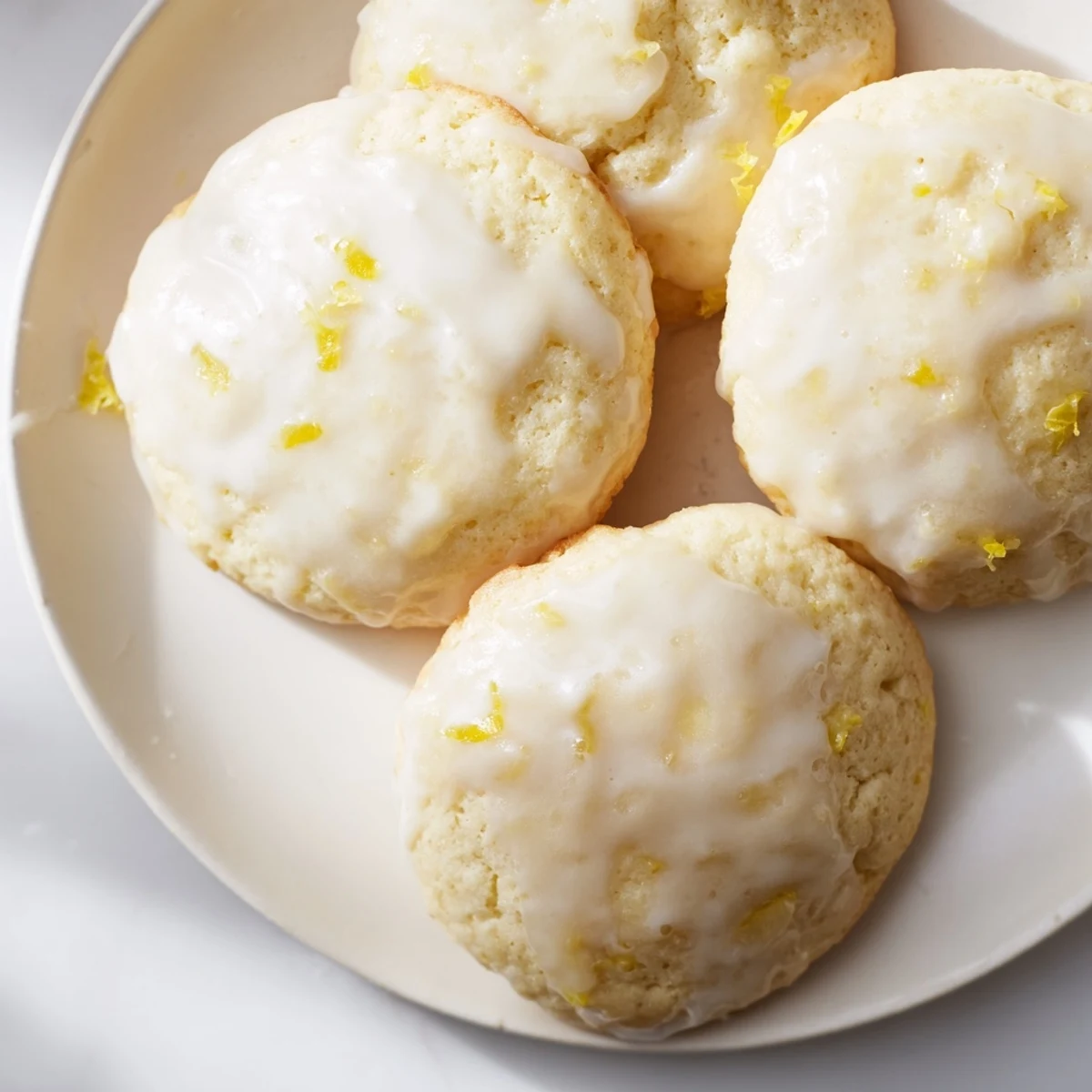Lemon Ricotta Cookies topped with zesty glaze and lemon zest, stacked on a white plate for a bright dessert display.