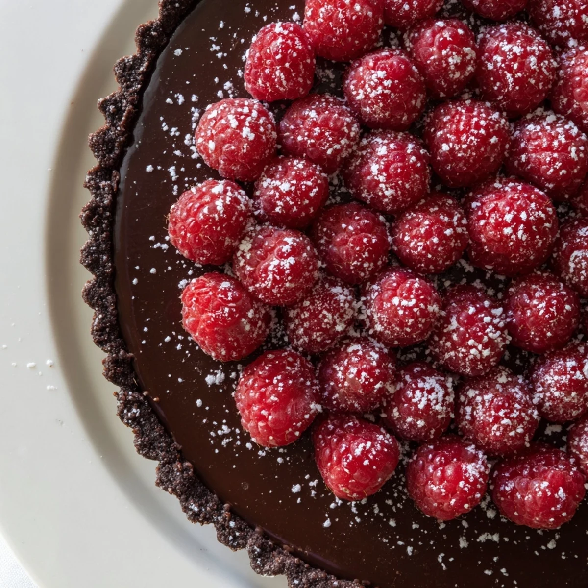 Serving a Chocolate Raspberry Tart dusted with powdered sugar on a dessert plate with a fork.
