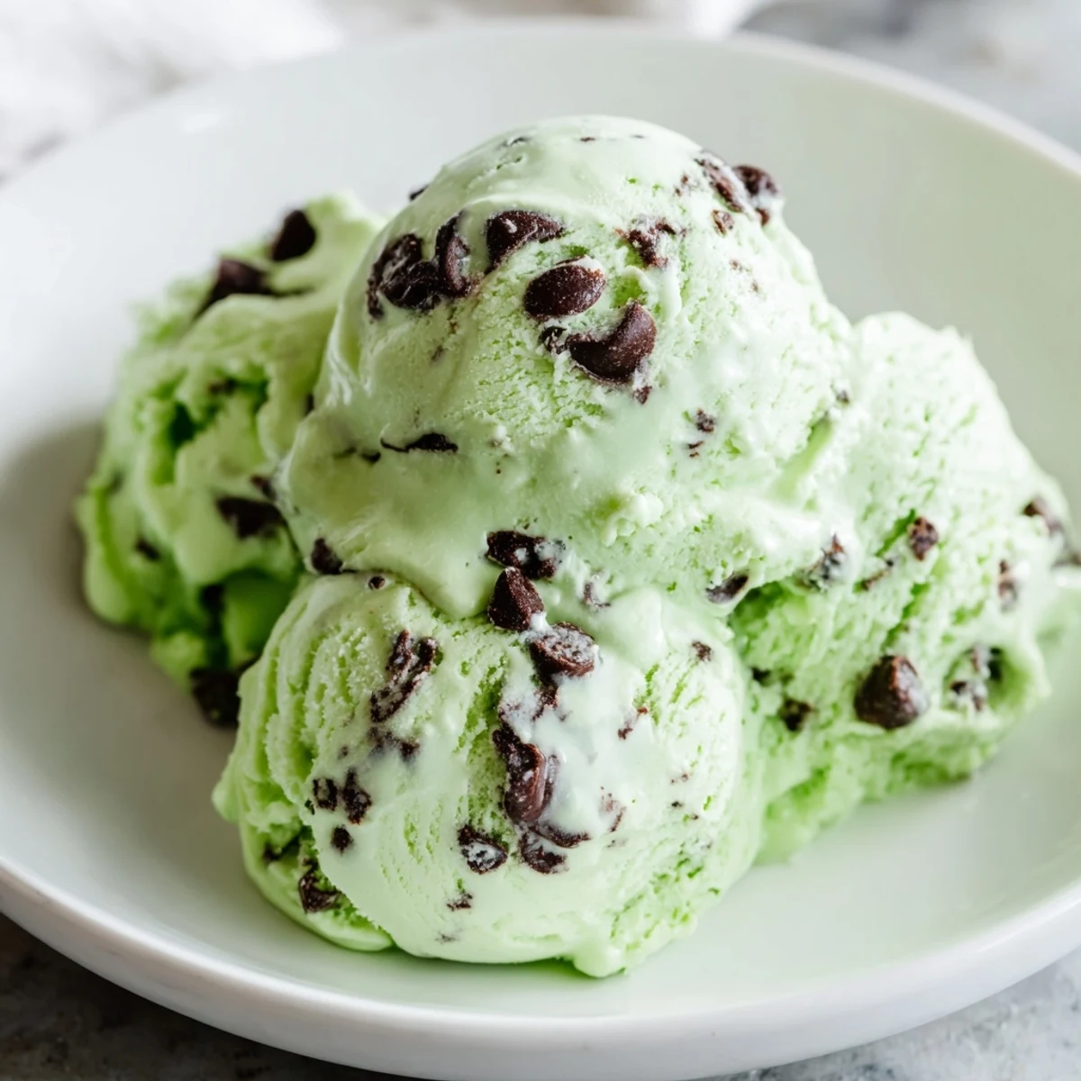 A frozen pint of homemade Green Mint Chocolate Chip Ice Cream resting on a marble countertop, condensation glistening on the container.