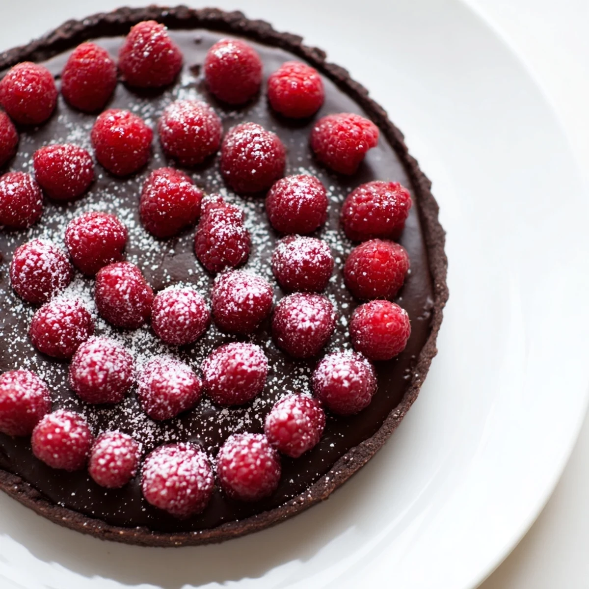 Close-up of a Chocolate Raspberry Tart with a dark, crackly chocolate crust filled with glossy ganache and topped with vibrant red raspberries.