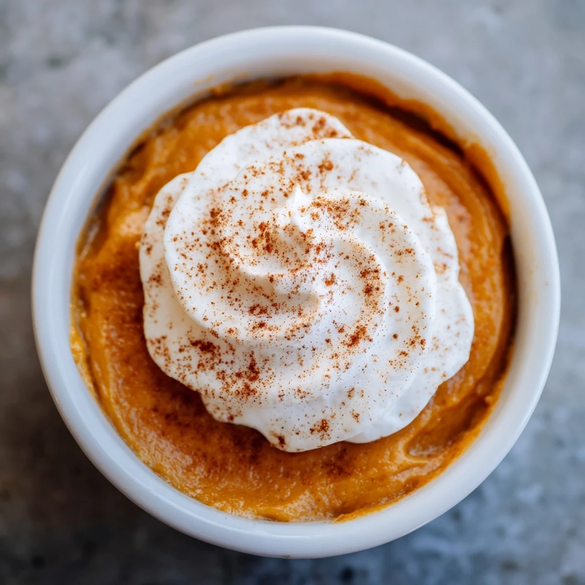 A single serving of Effortless Baked Pumpkin Pudding sits on a rustic wooden table, garnished with whipped cream.