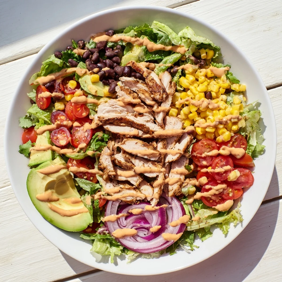 Sliced chipotle lime chicken salad on mixed greens with tomatoes, avocado, and black beans in a serving bowl.