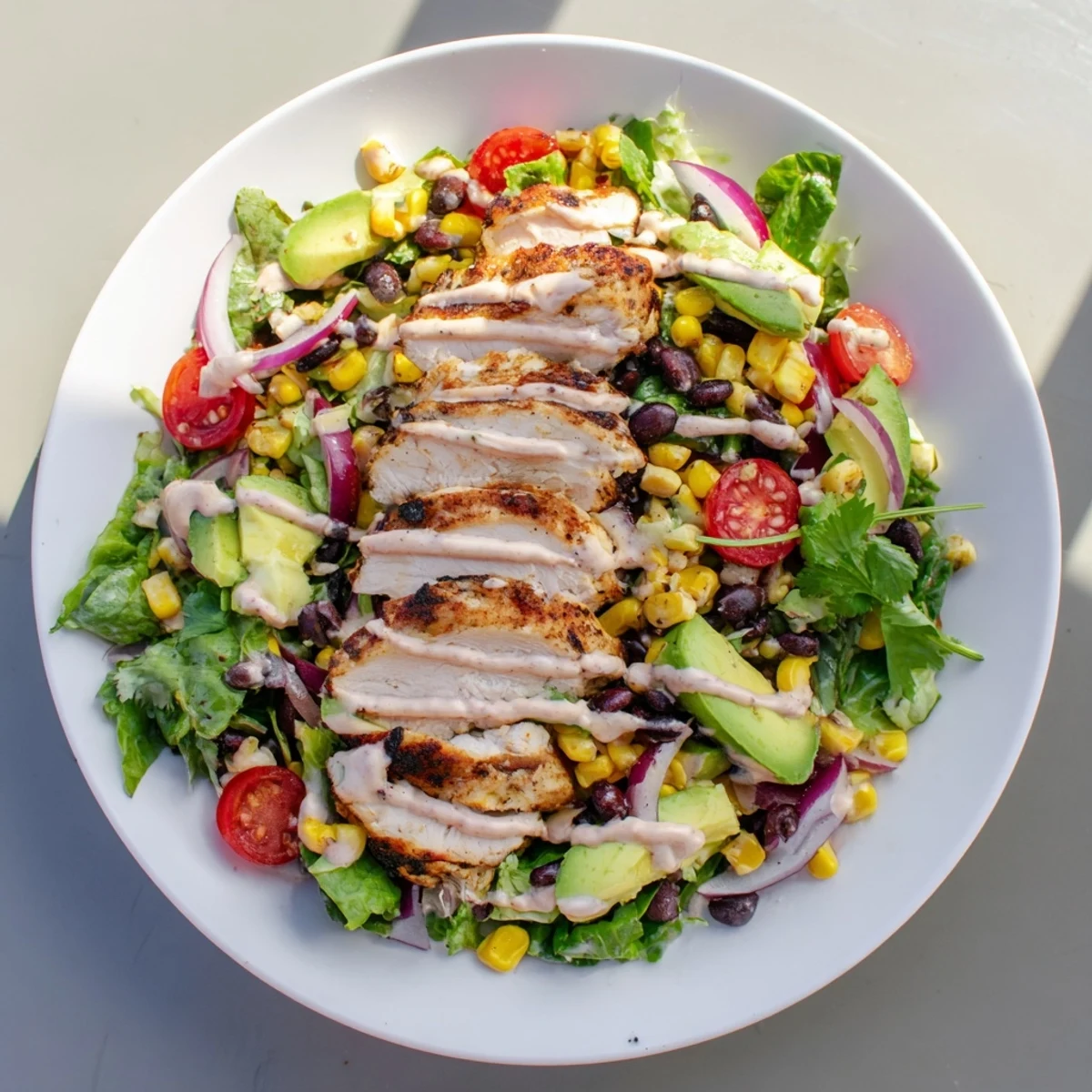 Freshly prepared chipotle lime chicken salad topped with corn and red onion, drizzled with tangy dressing on a plate.