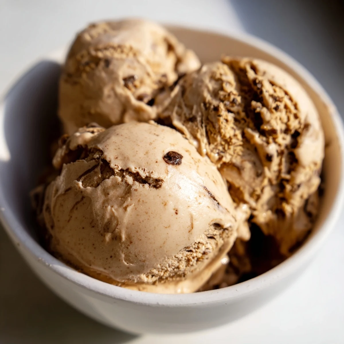 A scoop of Vietnamese Coffee Ice Cream in a glass bowl shows creamy texture and visible coffee flecks, served with a spoon.