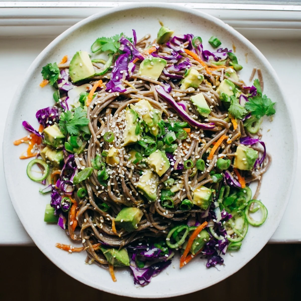Crisp sesame avocado and soba noodle salad served in a rustic bowl with lime wedge and colorful vegetables.