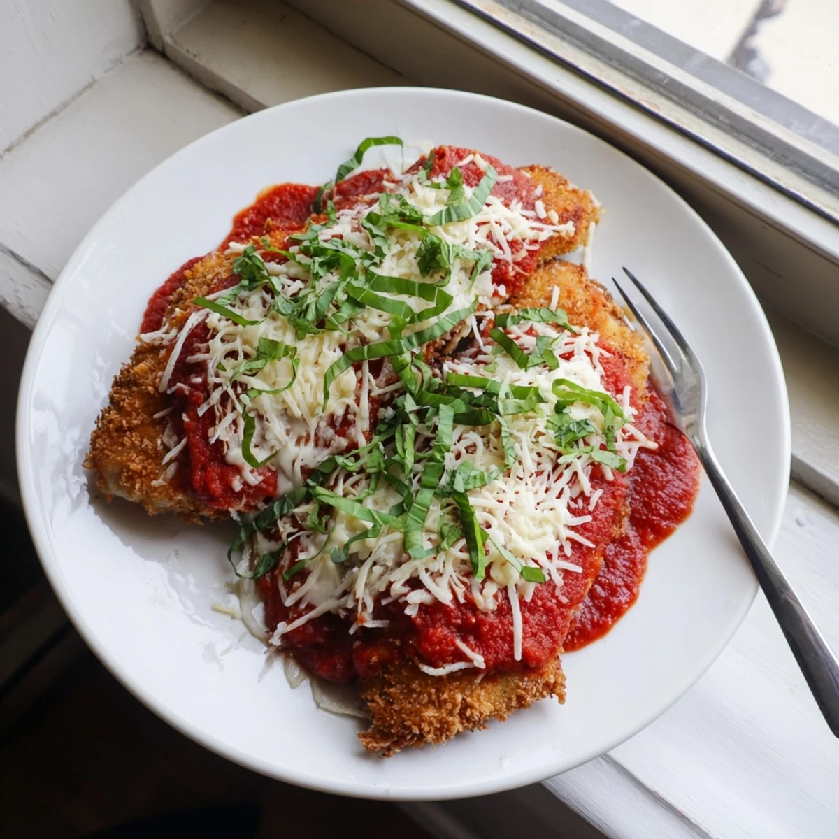 Crispy golden Chicken Parmigiana coated in herbs, topped with rich marinara and melted mozzarella, served hot.