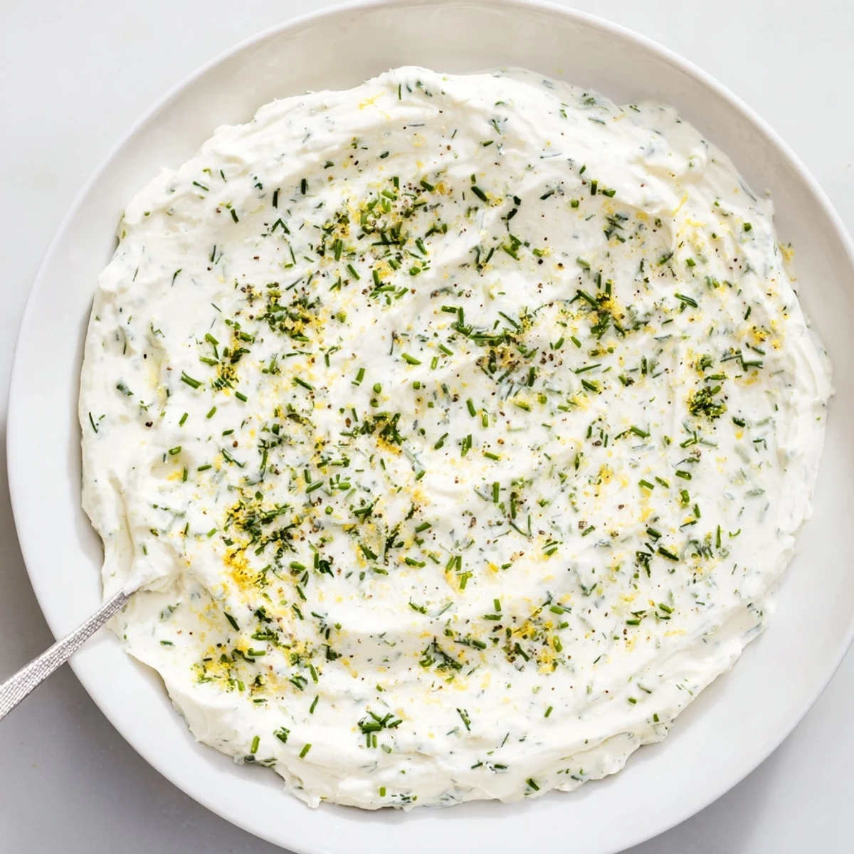 A creamy bowl of Simple Easter Herb Cheese Dip garnished with fresh chives, dill, and radish slices served with crackers.