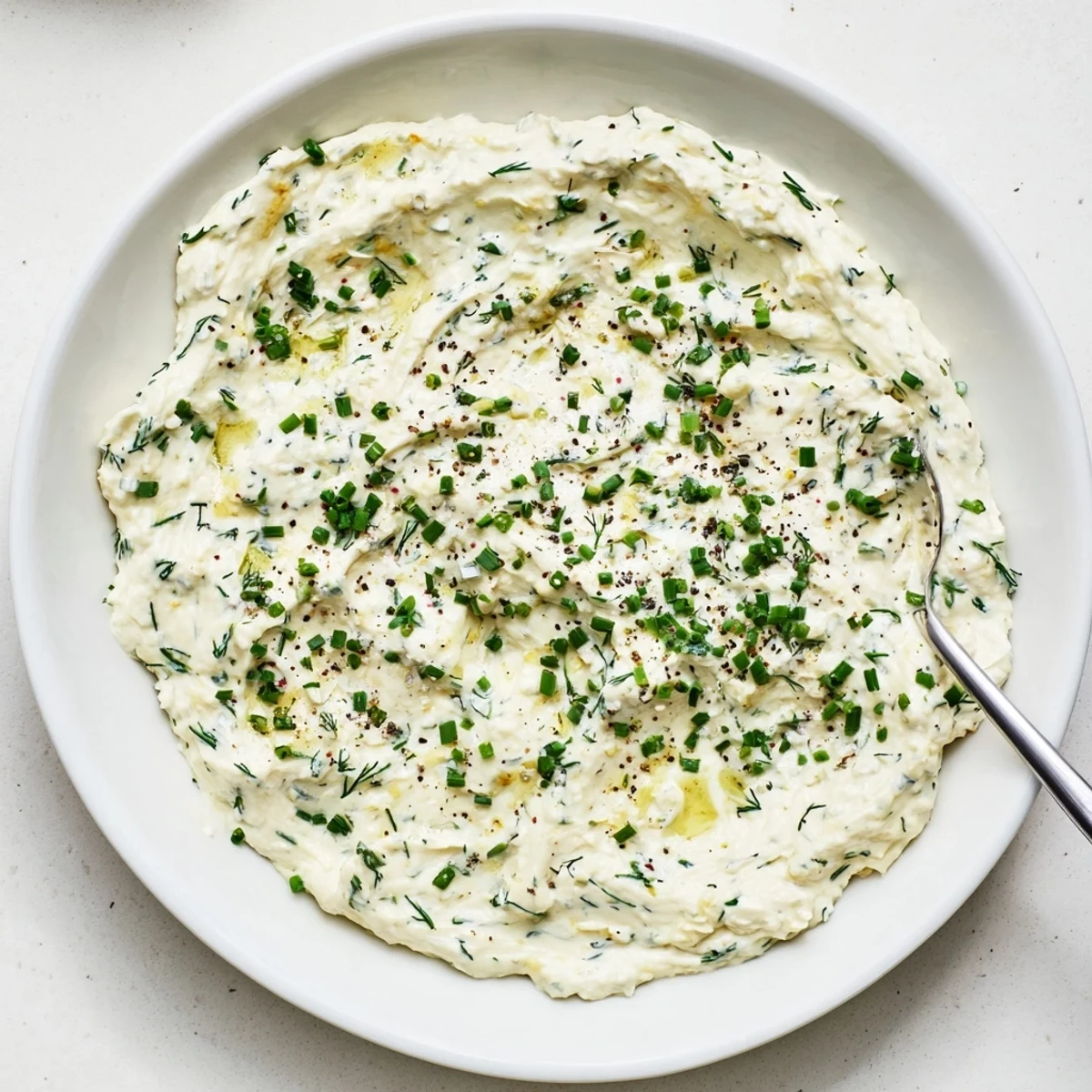 Close-up of Simple Easter Herb Cheese Dip made with cream cheese and cheddar, topped with herbs and lemon zest in a ceramic bowl.