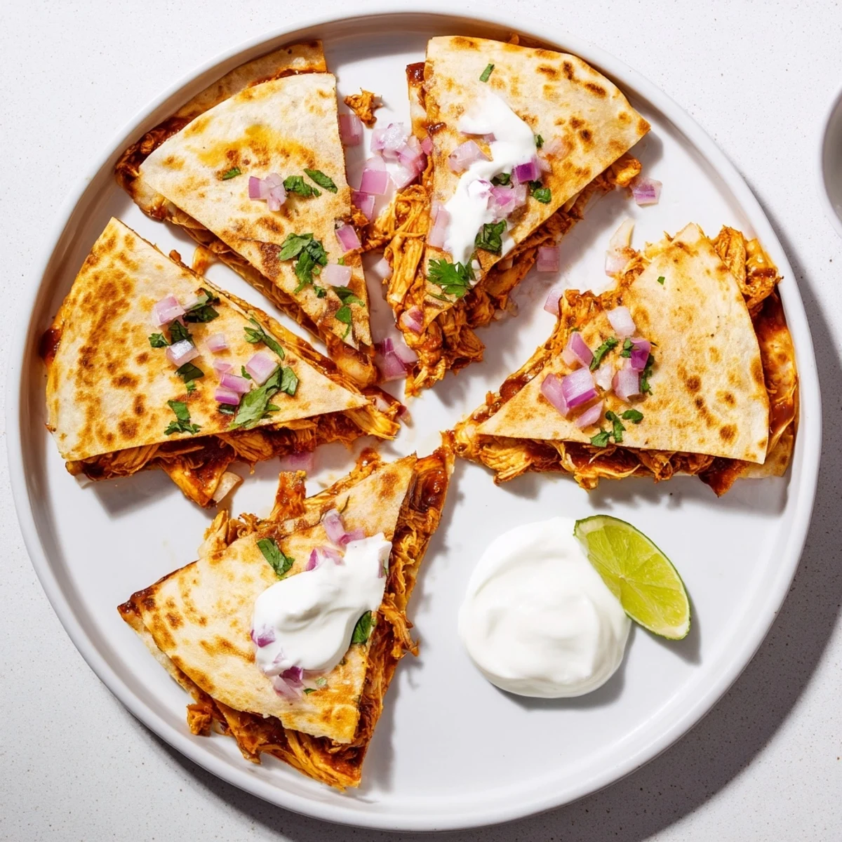 Overhead view of Hot Honey BBQ Chicken Quesadillas plated with a side of sour cream, lime wedges, and a drizzle of extra hot honey BBQ sauce.