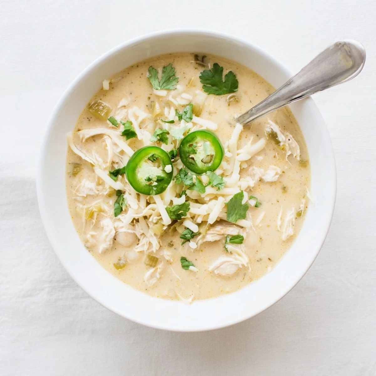 Creamy white chicken chili served in a bowl topped with fresh cilantro and jalapeño slices