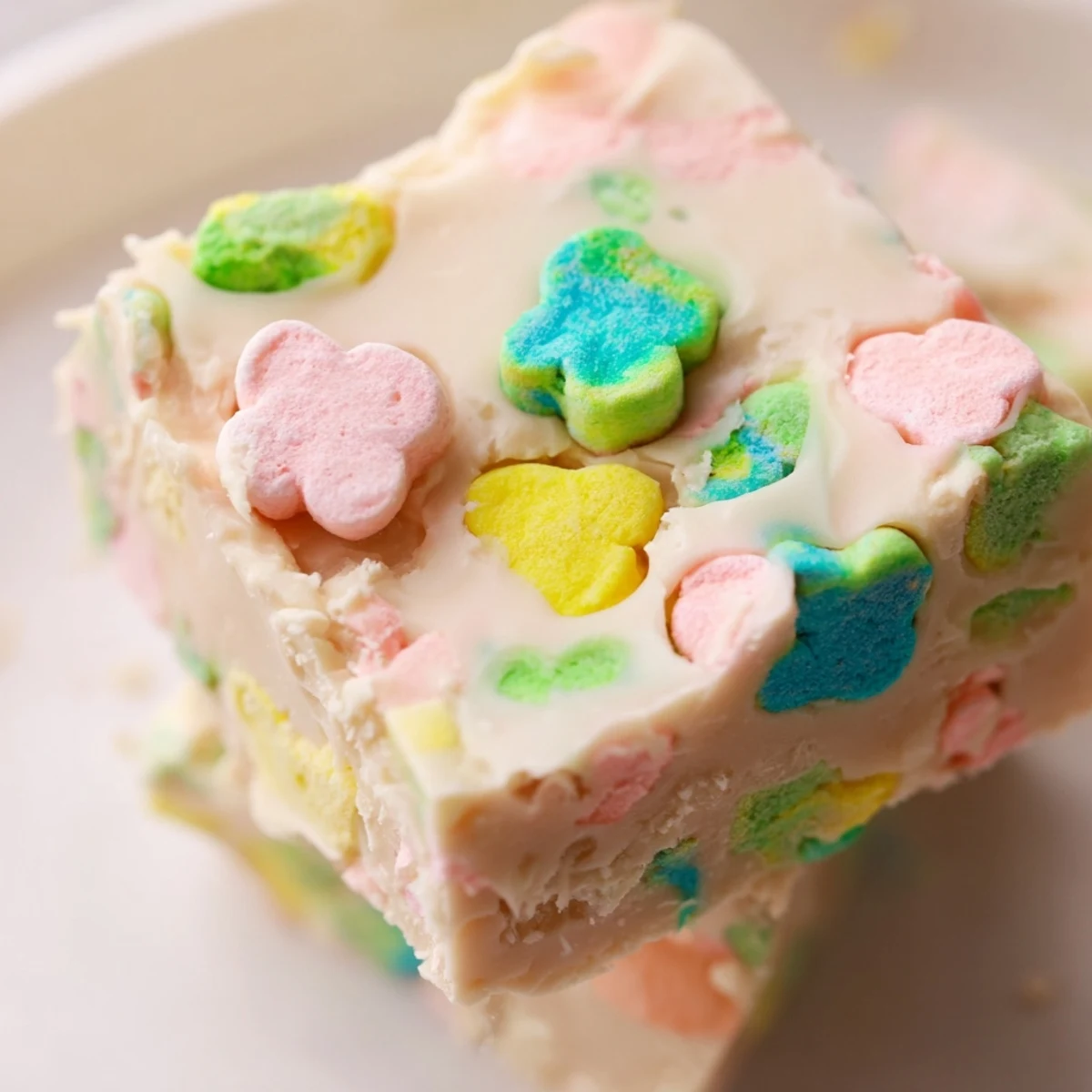 Creamy white chocolate Easy Lucky Charms Fudge topped with colorful rainbow marshmallows on a white plate