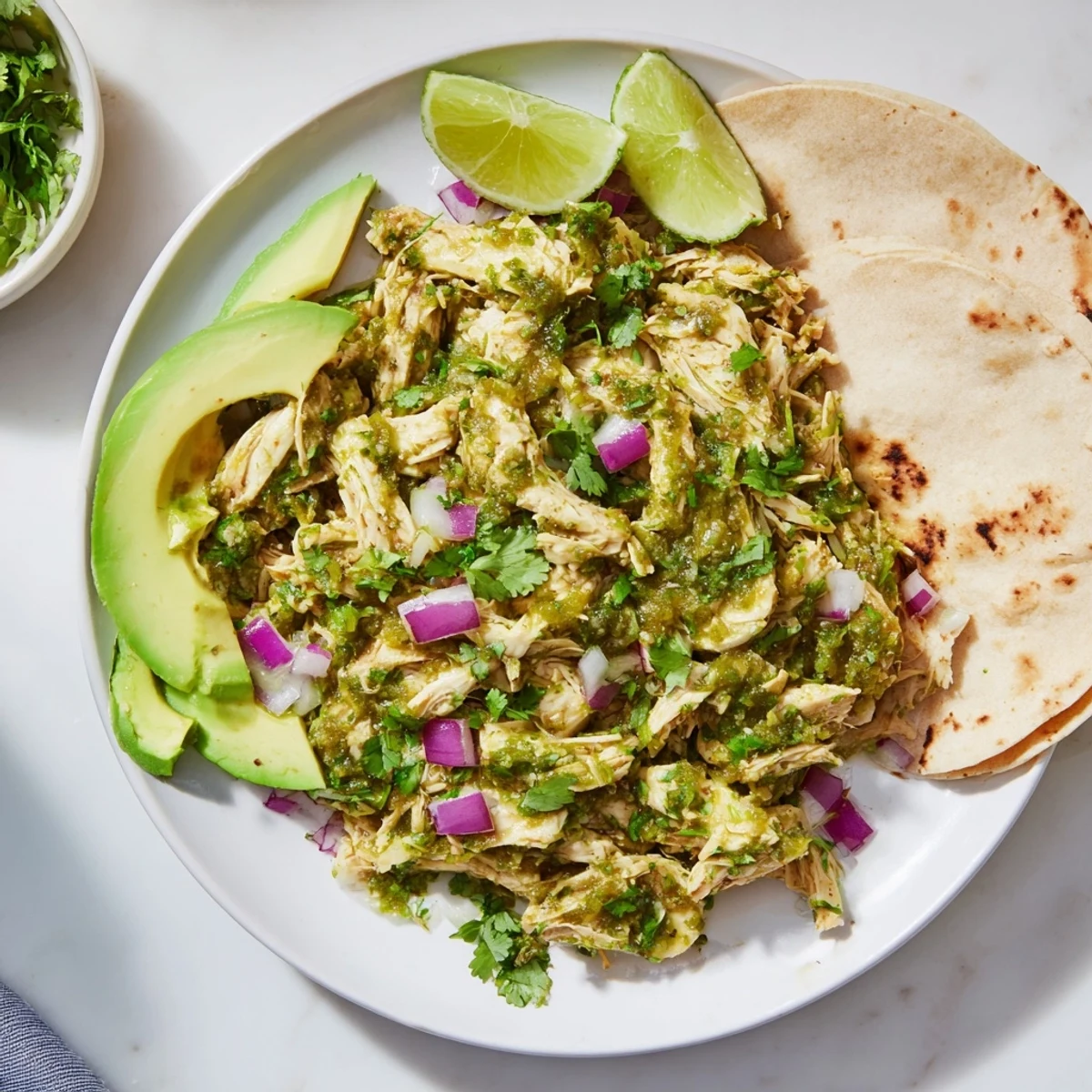 Salsa verde chicken topped with creamy avocado slices and lime wedges for Taco Tuesday dinner
