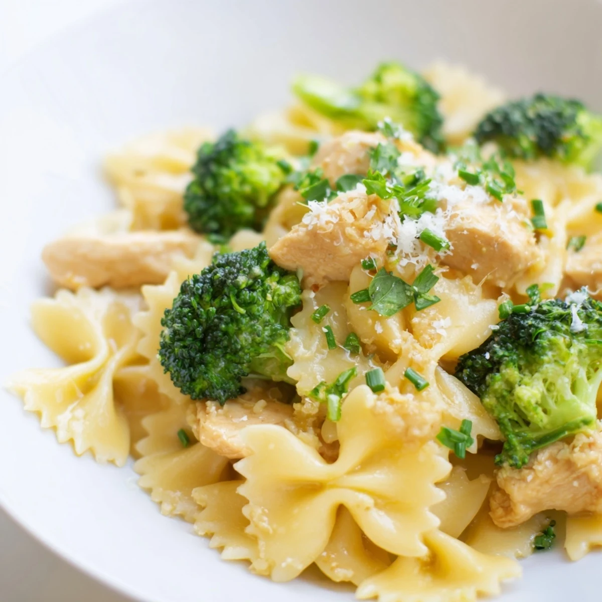 Creamy cowboy butter lemon chicken pasta bowl featuring farfalle, green broccoli florets, red onion slices, and golden parmesan garnish