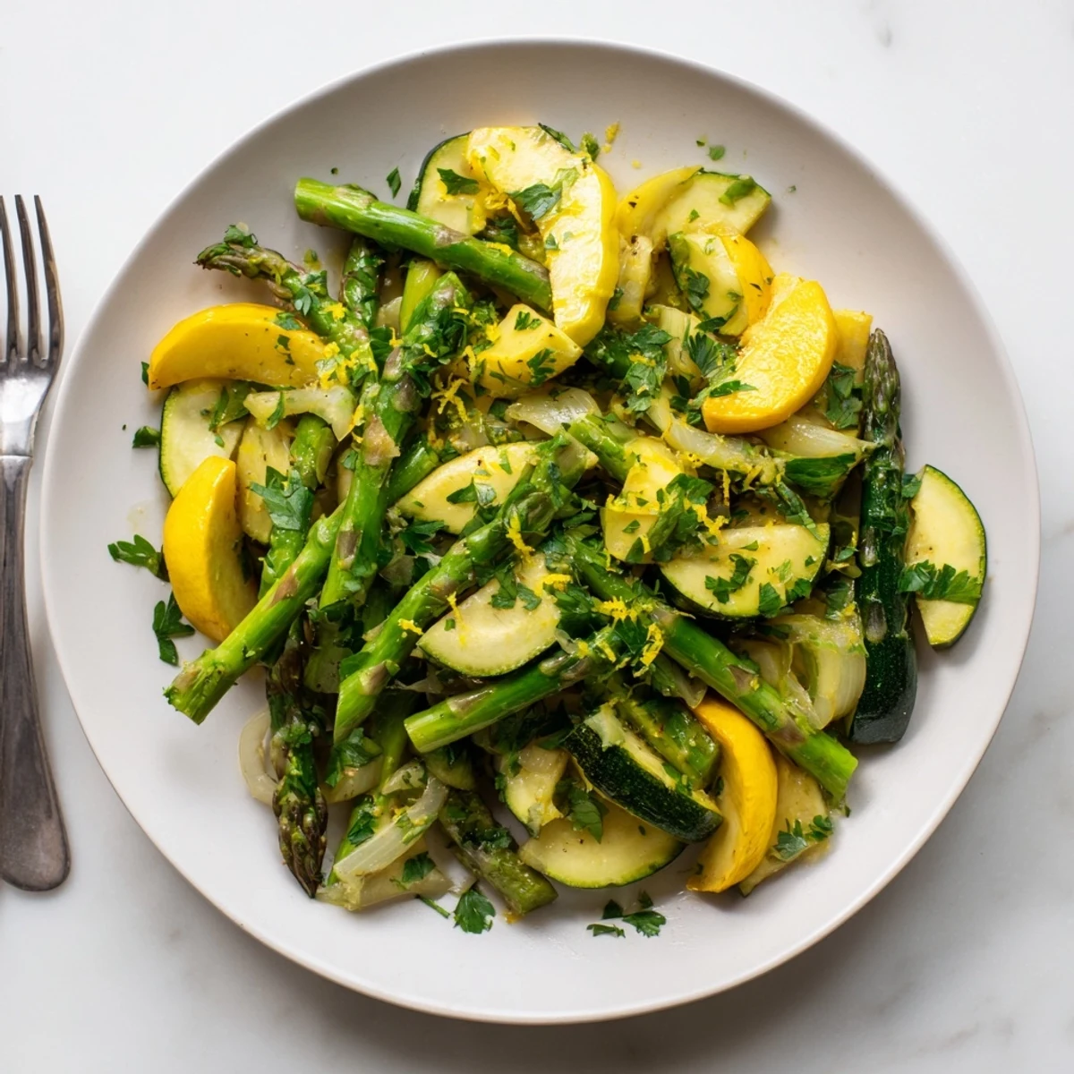 Golden sautéed asparagus with zucchini and yellow squash in a skillet, garnished with fresh parsley and lemon zest