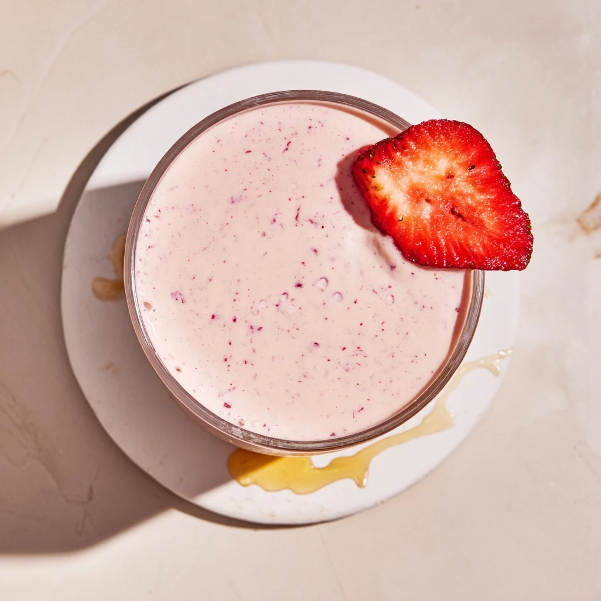 Pink strawberry yogurt smoothie poured into tall glass with strawberry on rim