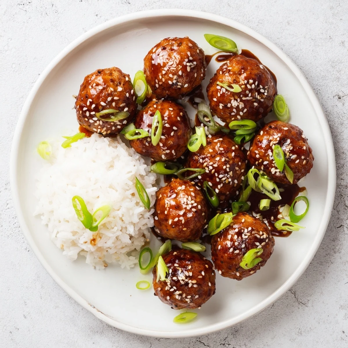 Juicy teriyaki chicken meatballs arranged on a white plate garnished with fresh sliced green onions