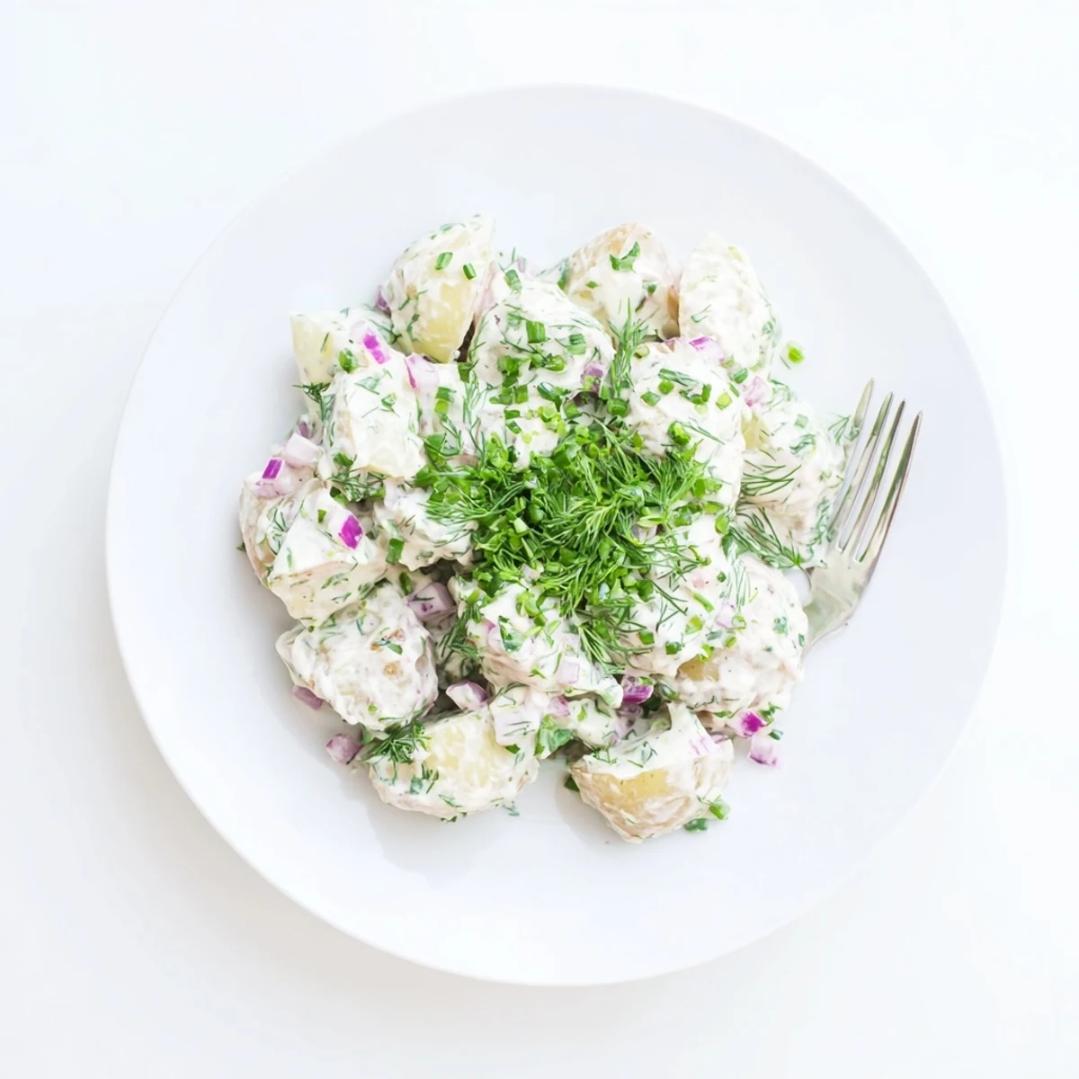 Creamy Greek yogurt potato salad with tender red potatoes, crisp celery, and fresh green herbs in a white serving bowl