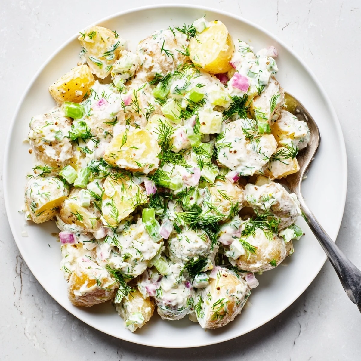 Golden potato chunks coated in tangy Greek yogurt dressing with colorful vegetables and chopped herbs for summer picnics