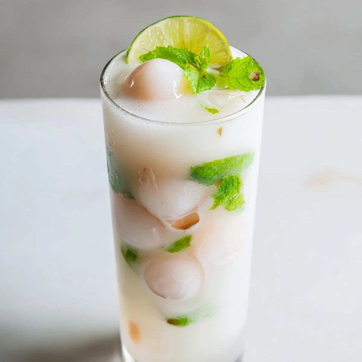 Frosty glass of coconut lychee iced drink topped with mint leaves on wooden table