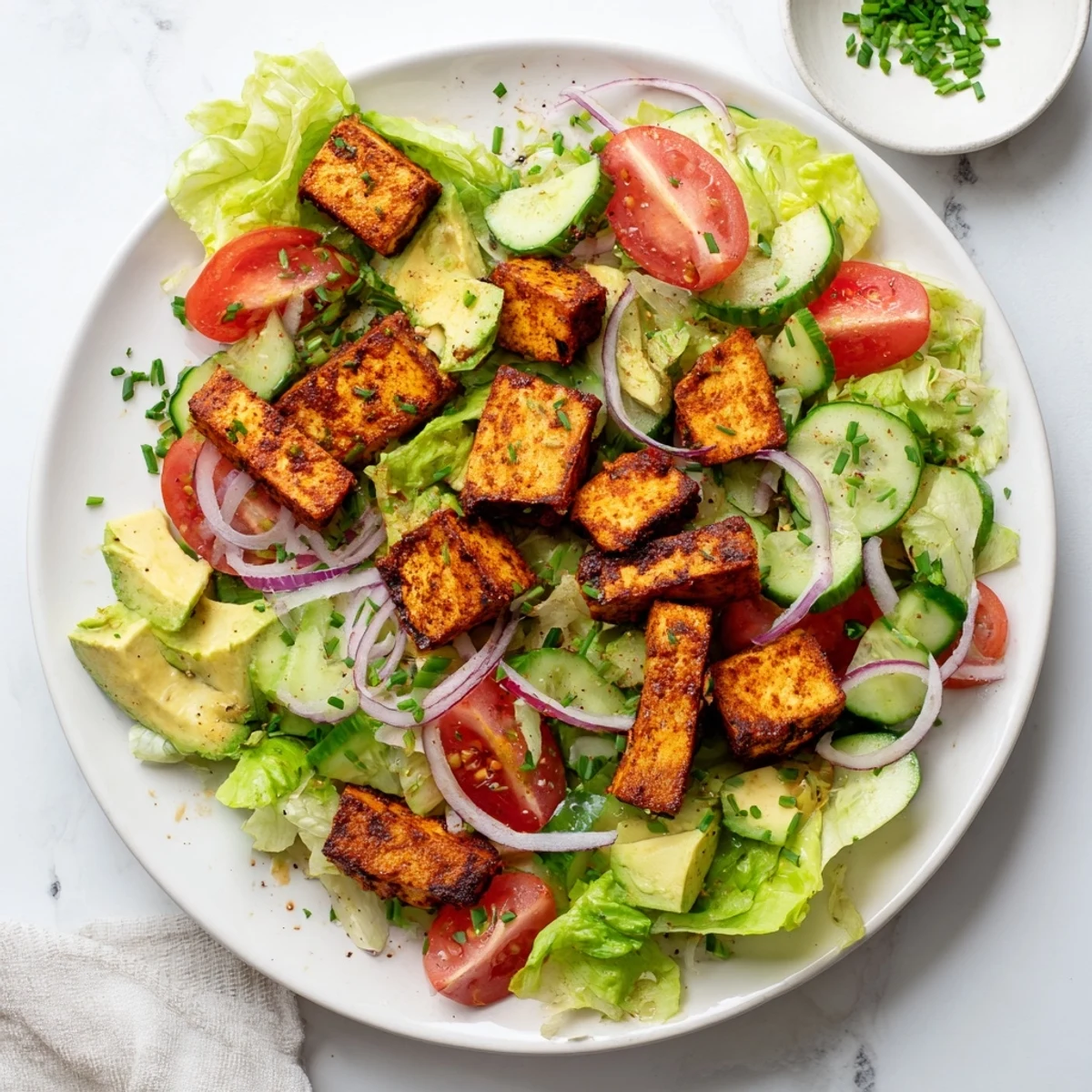 Golden smoky tofu pieces atop crisp lettuce and juicy ripe tomatoes in a summer bowl