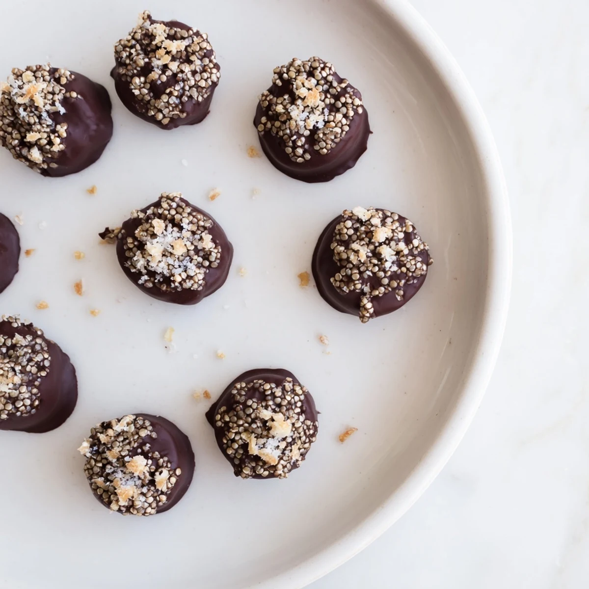 Dark chocolate quinoa crisps arranged on a white plate with a sprinkle of sea salt