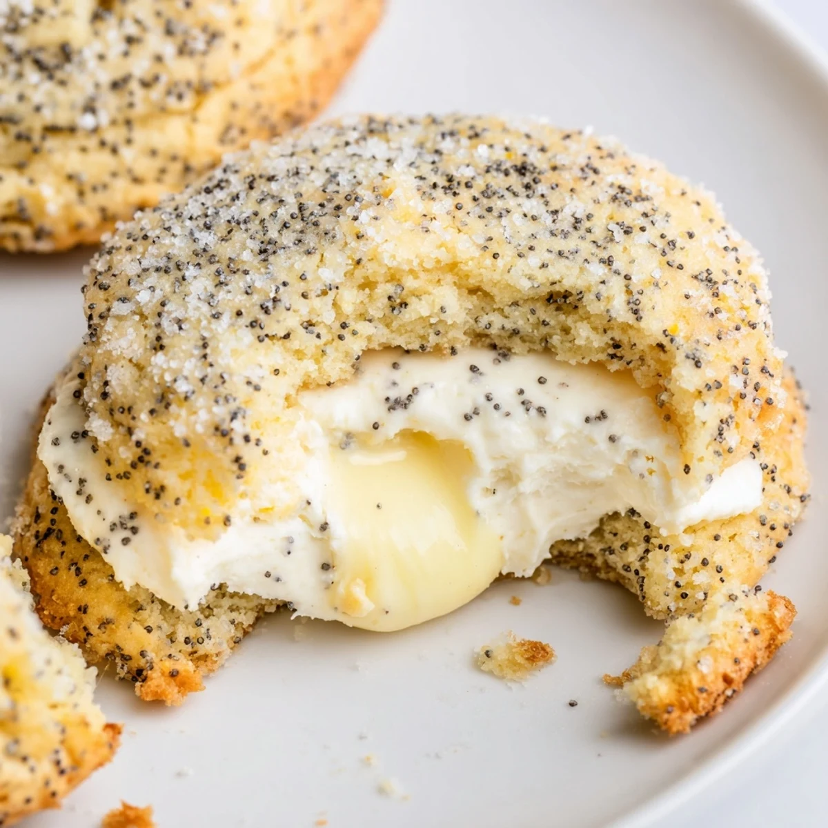 Soft-baked lemon poppy seed cheesecake cookies oozing tangy filling on white plate