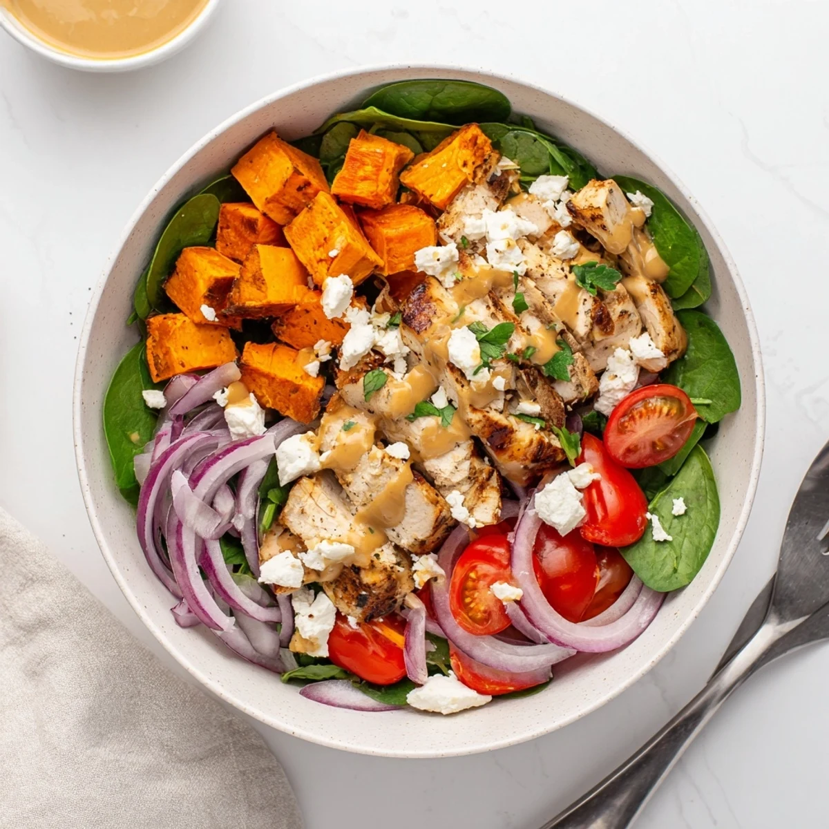 Colorful meal prep bowl featuring maple Dijon chicken, caramelized sweet potato pieces, crisp greens, and crumbled feta cheese topping.