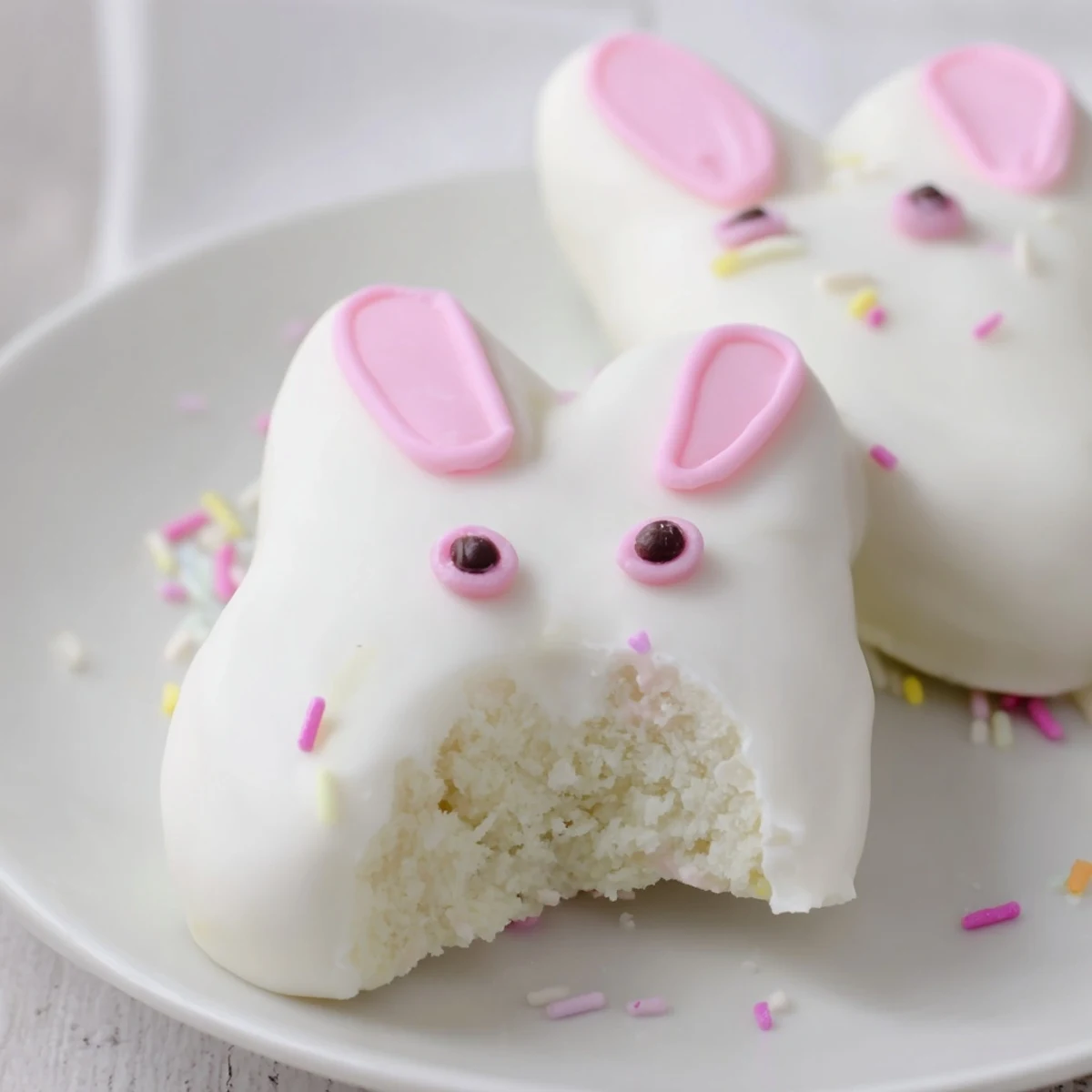 Creamy white chocolate bunny cakesicles decorated with pink ears and colorful spring sprinkles