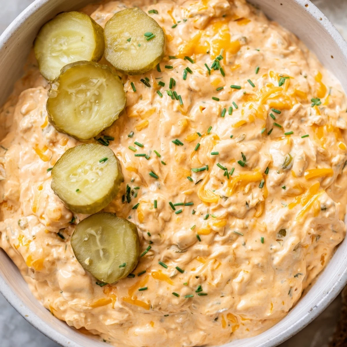 Creamy buffalo pickle dip in a serving bowl surrounded by crispy chips and fresh veggie sticks