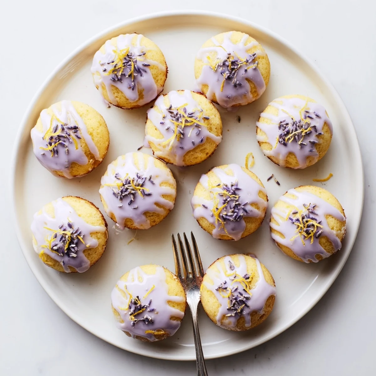 A batch of mini lemon cakes with lavender glaze set on a pastel cake stand