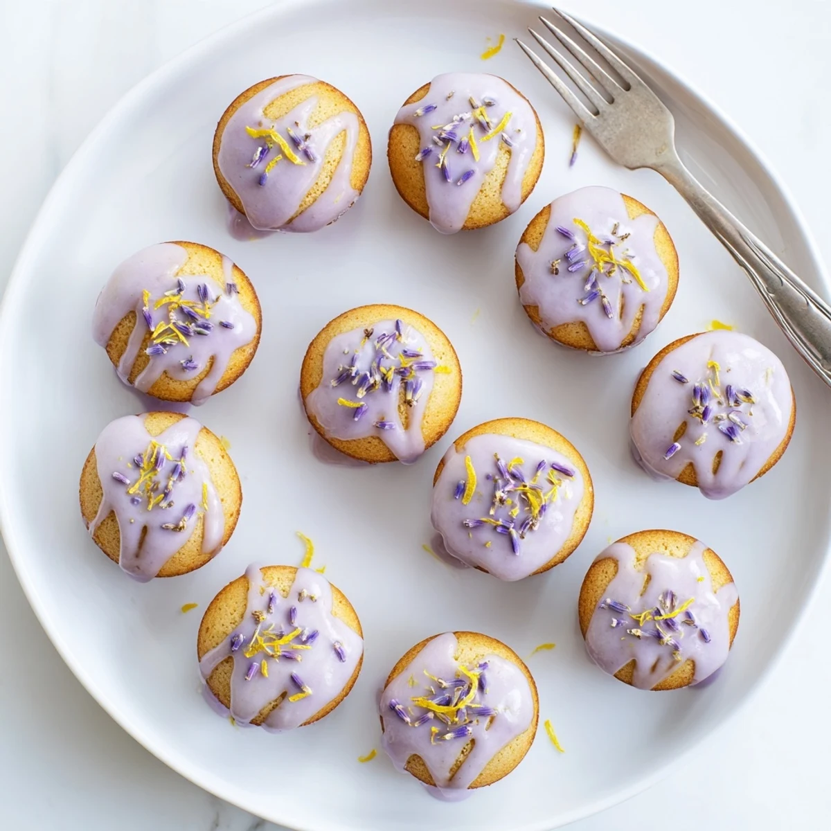 Soft mini lemon cakes topped with purple-dotted lavender glaze on a white dessert plate