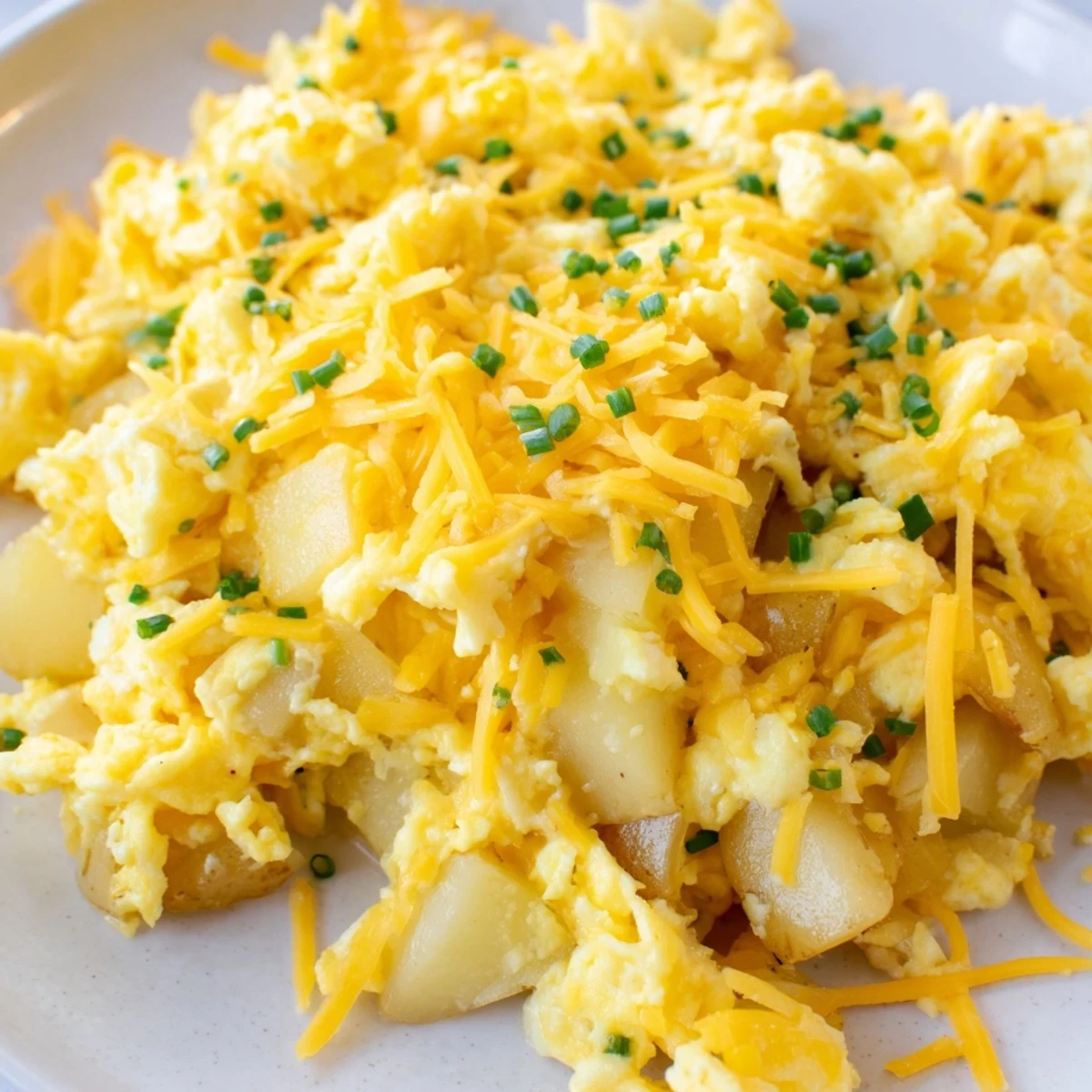Golden cheesy potato egg scramble plated with fluffy eggs and melted cheddar cheese topping
