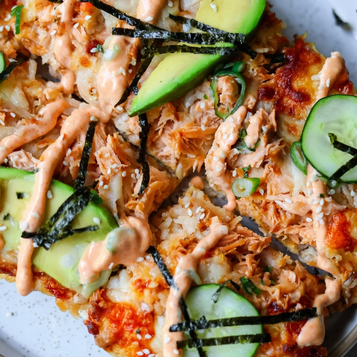 Salmon sushi bake pizza drizzled with spicy mayo and topped with fresh avocado slices
