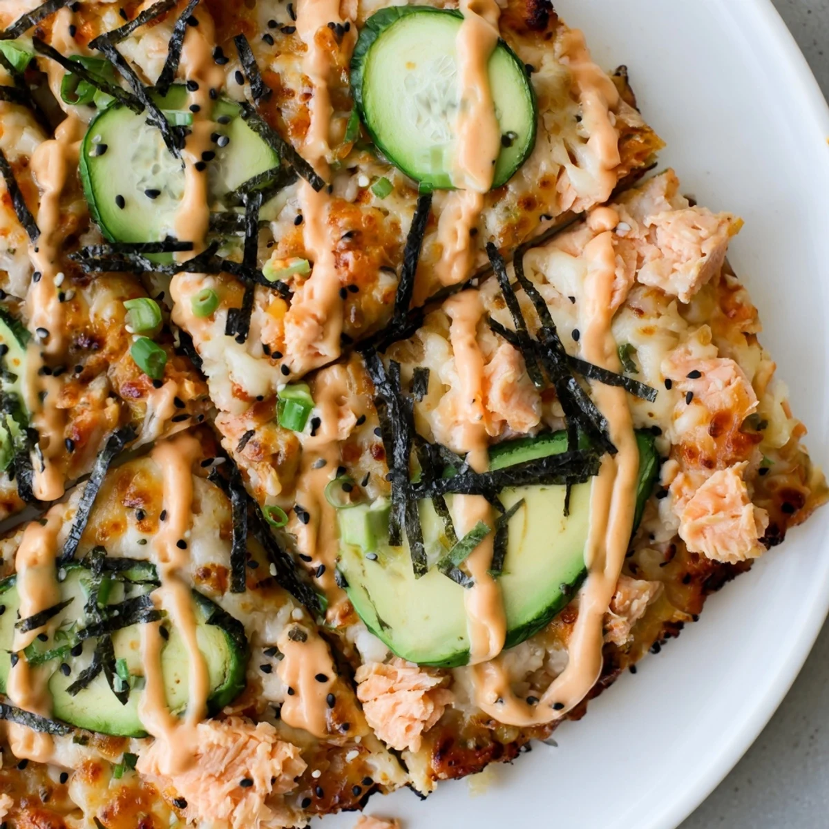 Fusion flatbread featuring seasoned salmon, rice, and vegetables with a bold spicy sriracha sauce