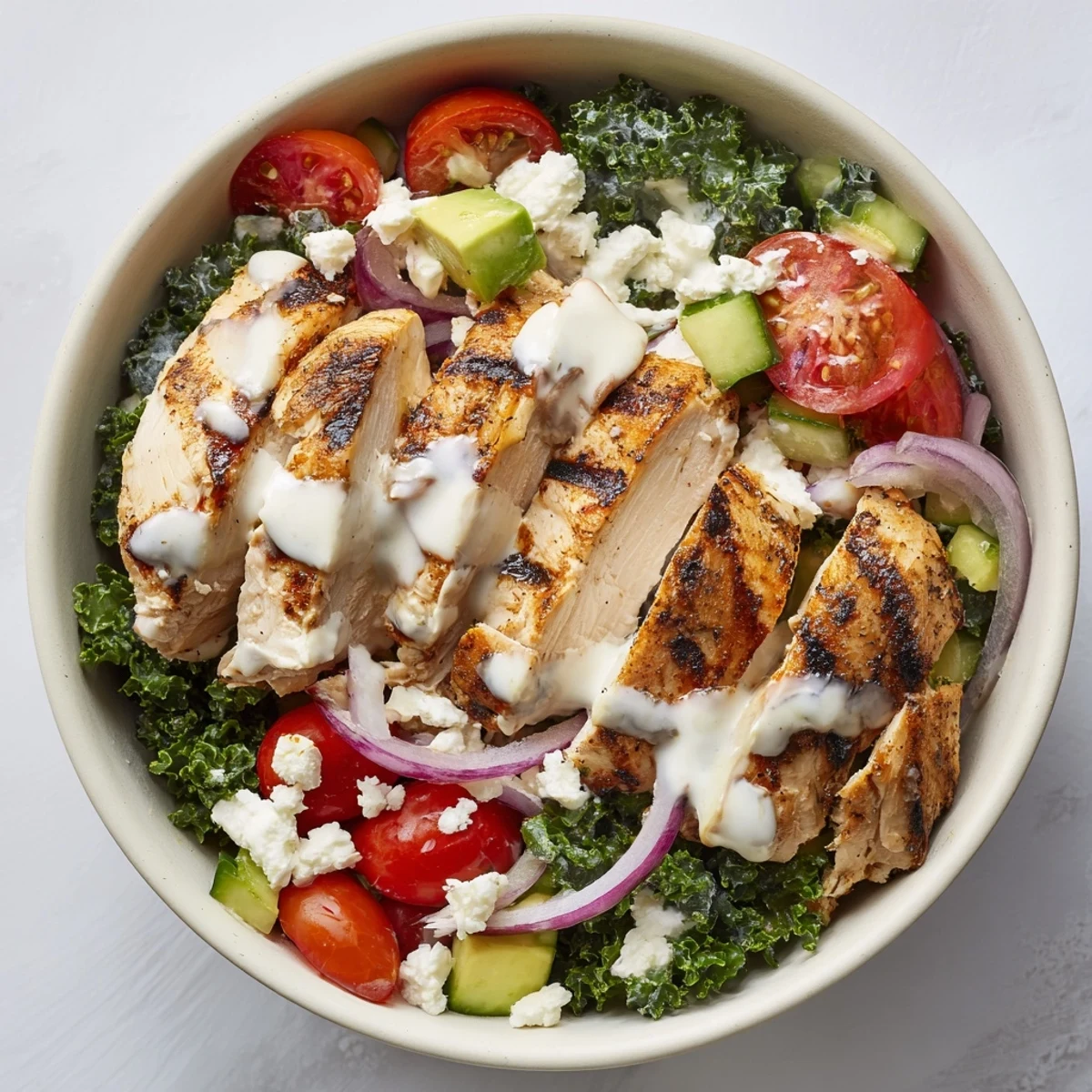 Wholesome marinated kale and chicken bowl featuring avocado, red onion, and tangy yogurt dressing